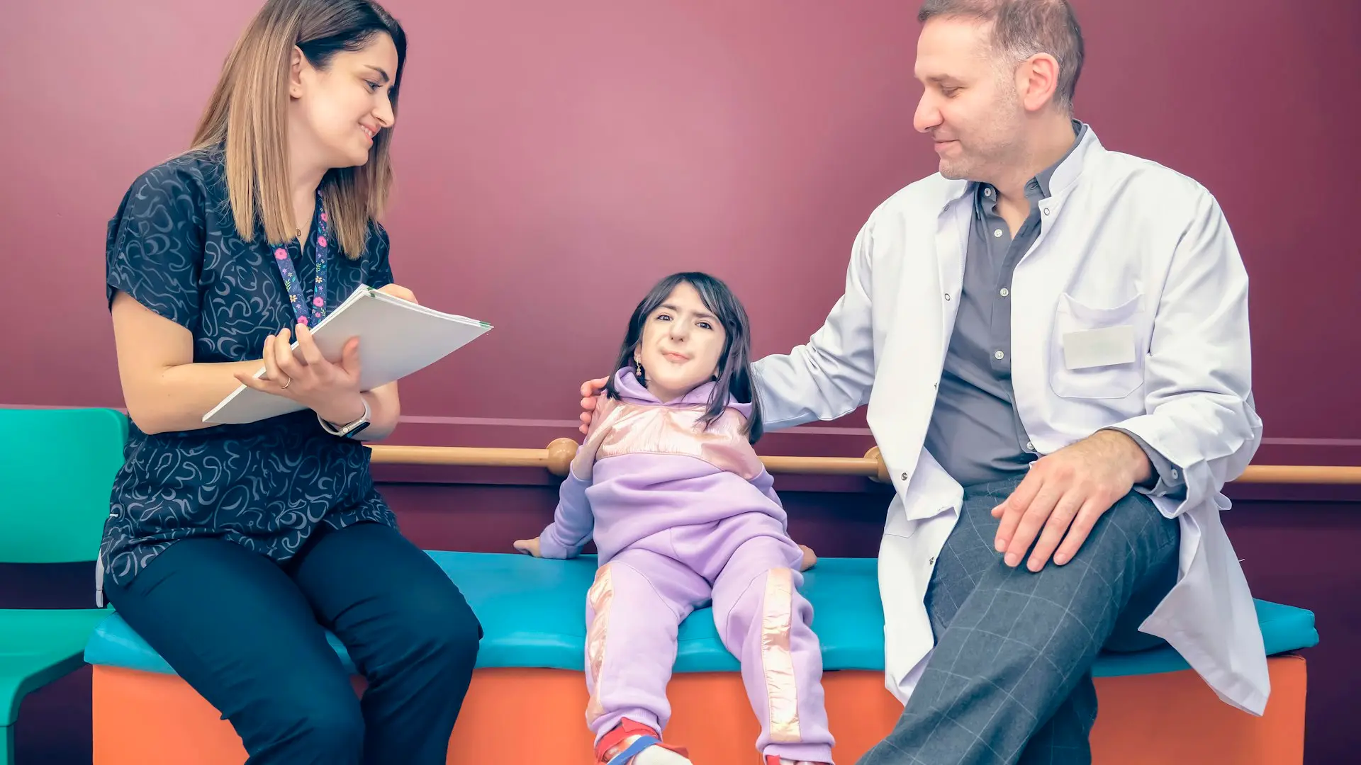 Two pediatric providers sit with a young girl on a colorful bench in the clinic